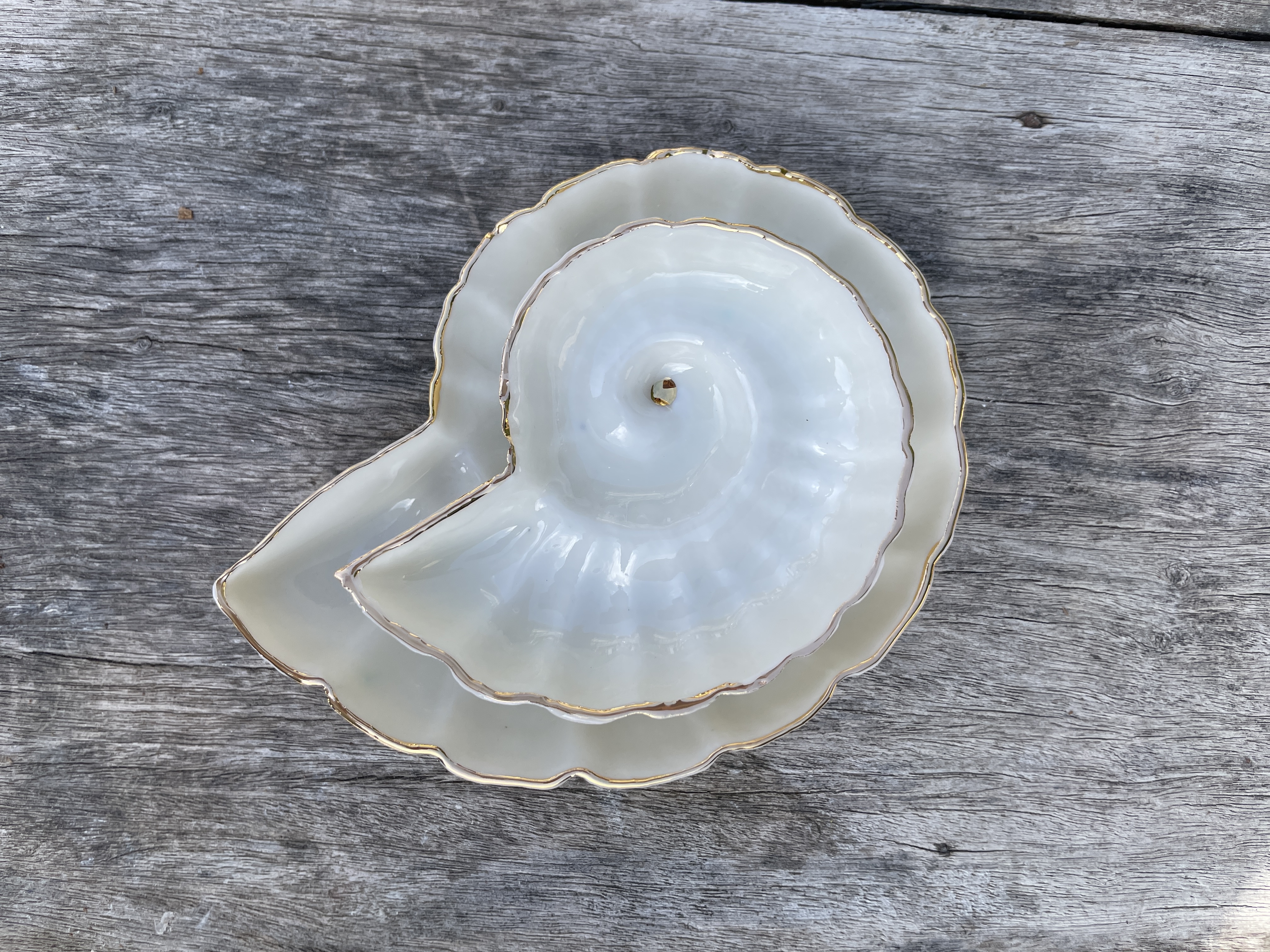 Weiße Keramikschale in Spiralform mit Goldrand auf verwittertem Holz.